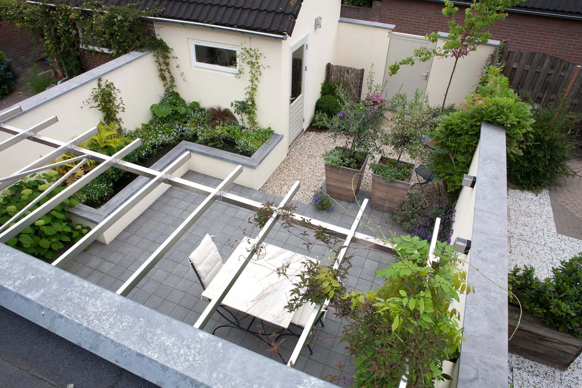 Luchtfoto van moderne buitenkamer met witte pergola, verhoogde plantenbakken en gestructureerde indeling
