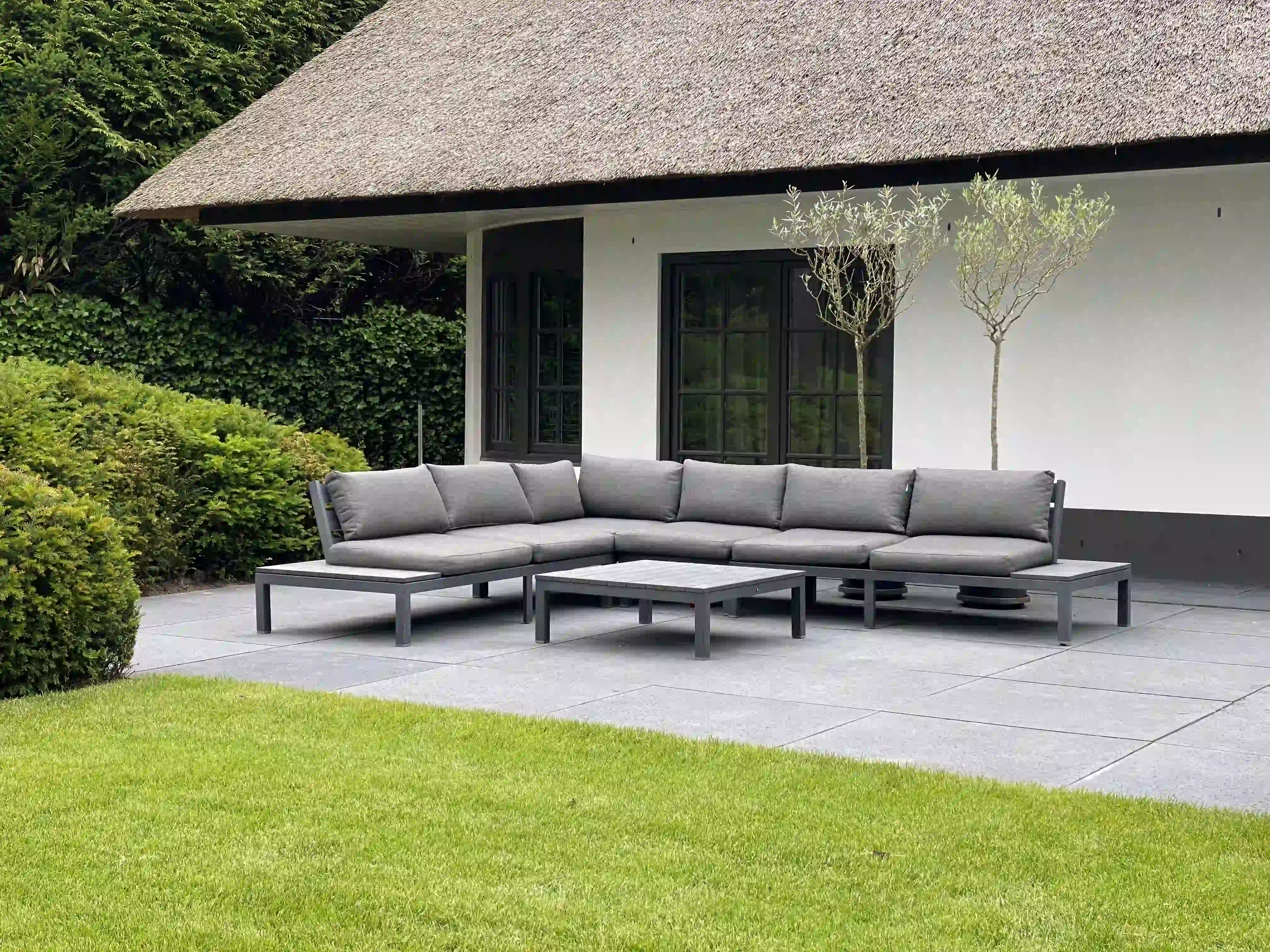Groot loungebank op terras voor traditionele boerderij met rieten dak