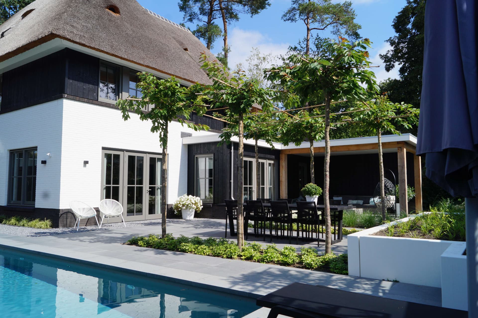 Moderne tuin met traditioneel rietgedekt huis, zwembad en overdekt terras met eetgedeelte
