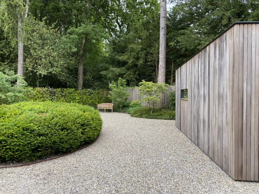 Grindpad door de tuin met houten schuur en vormgesnoeide buxus