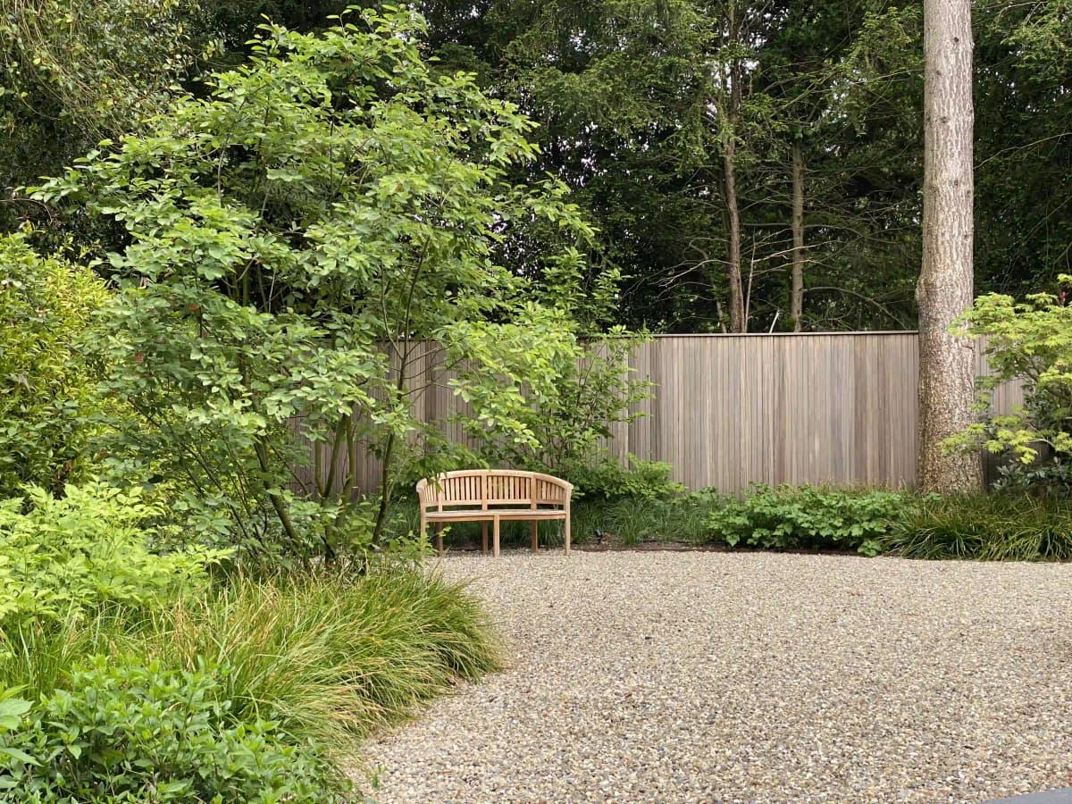 Houten tuinbank tussen natuurlijke beplanting met houten schutting