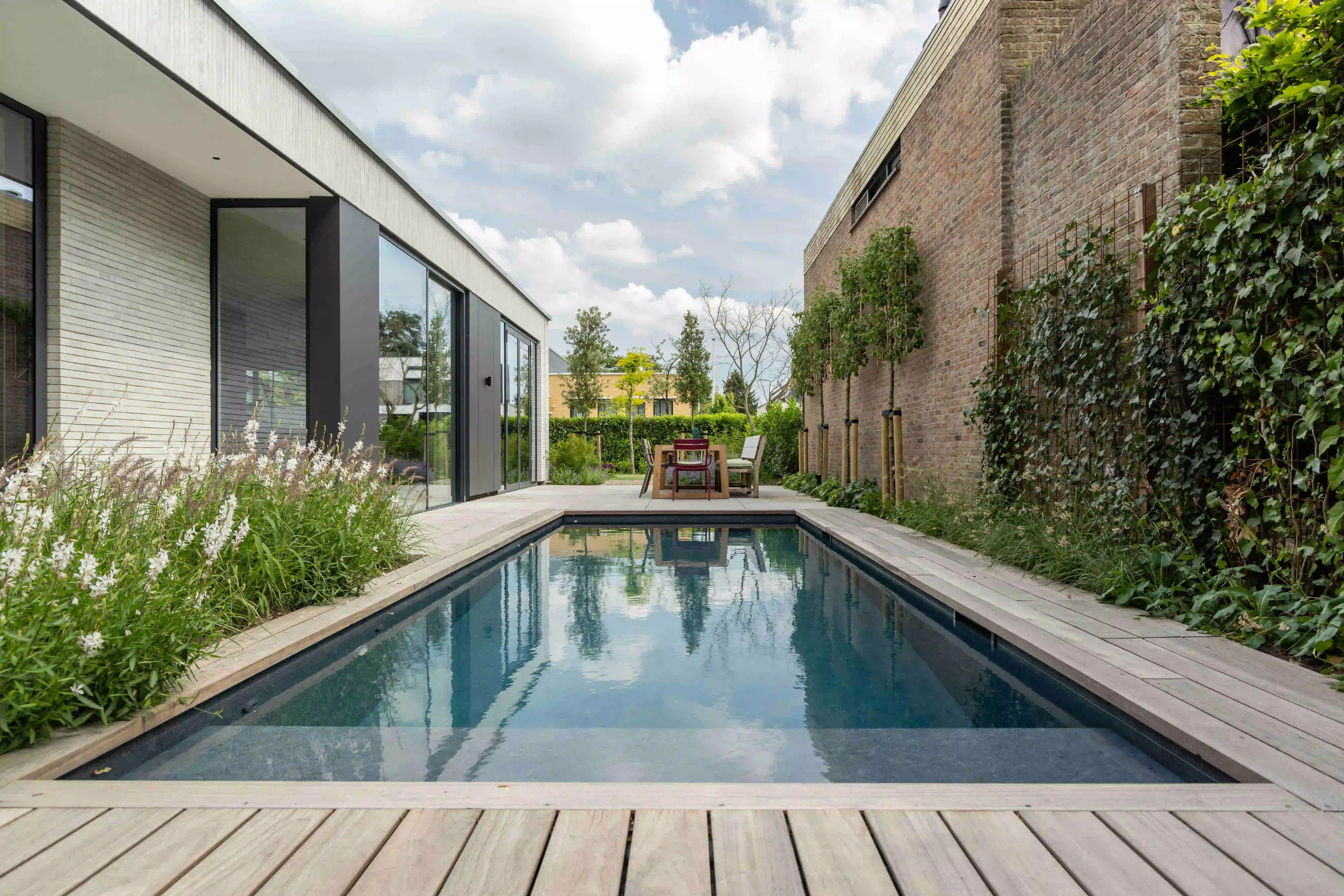 Pool view with wooden deck, dining area, and brick wall