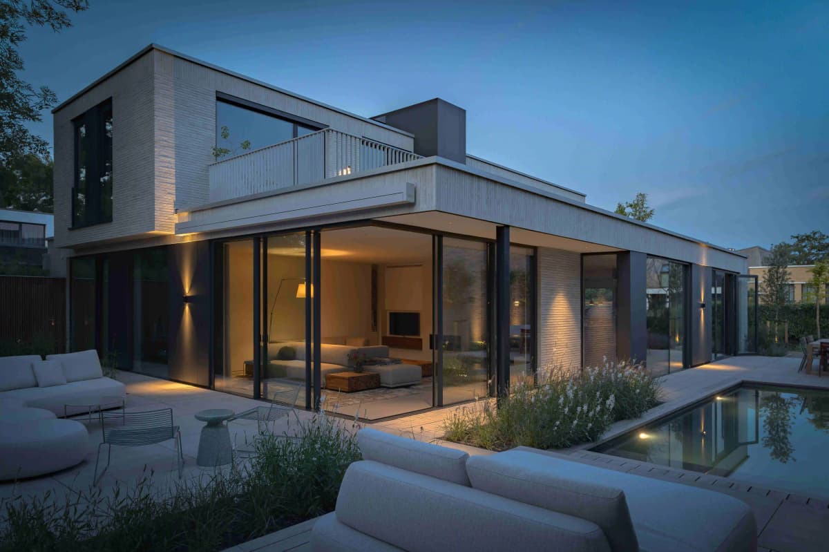 Wide evening view of modern house with rooftop terrace and illuminated garden
