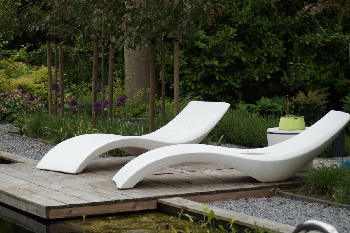Witte designligbedden op houten vlonder met paarse allium bloemen en bomen
