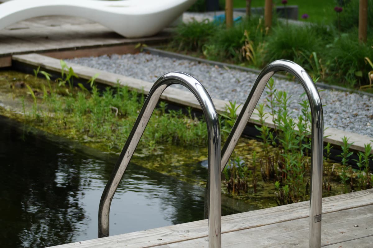 Detail van roestvrijstalen zwembadladder in natuurlijke zwemvijver