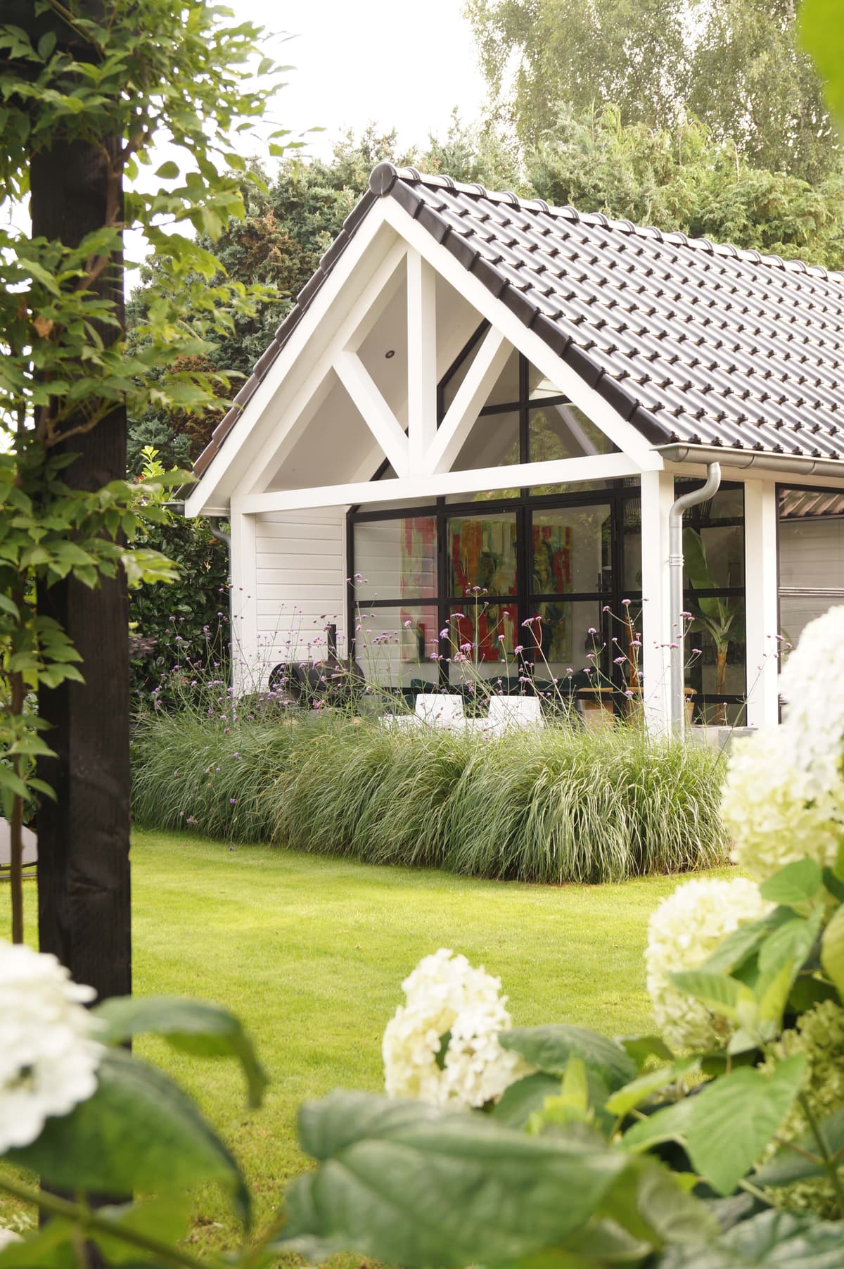 Buitenaanzicht tuinhuis met witte hortensia's en siergrassen