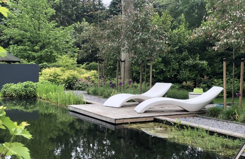 Ligbedden op houten vlonder naast natuurlijke zwemvijver met weelderige beplanting
