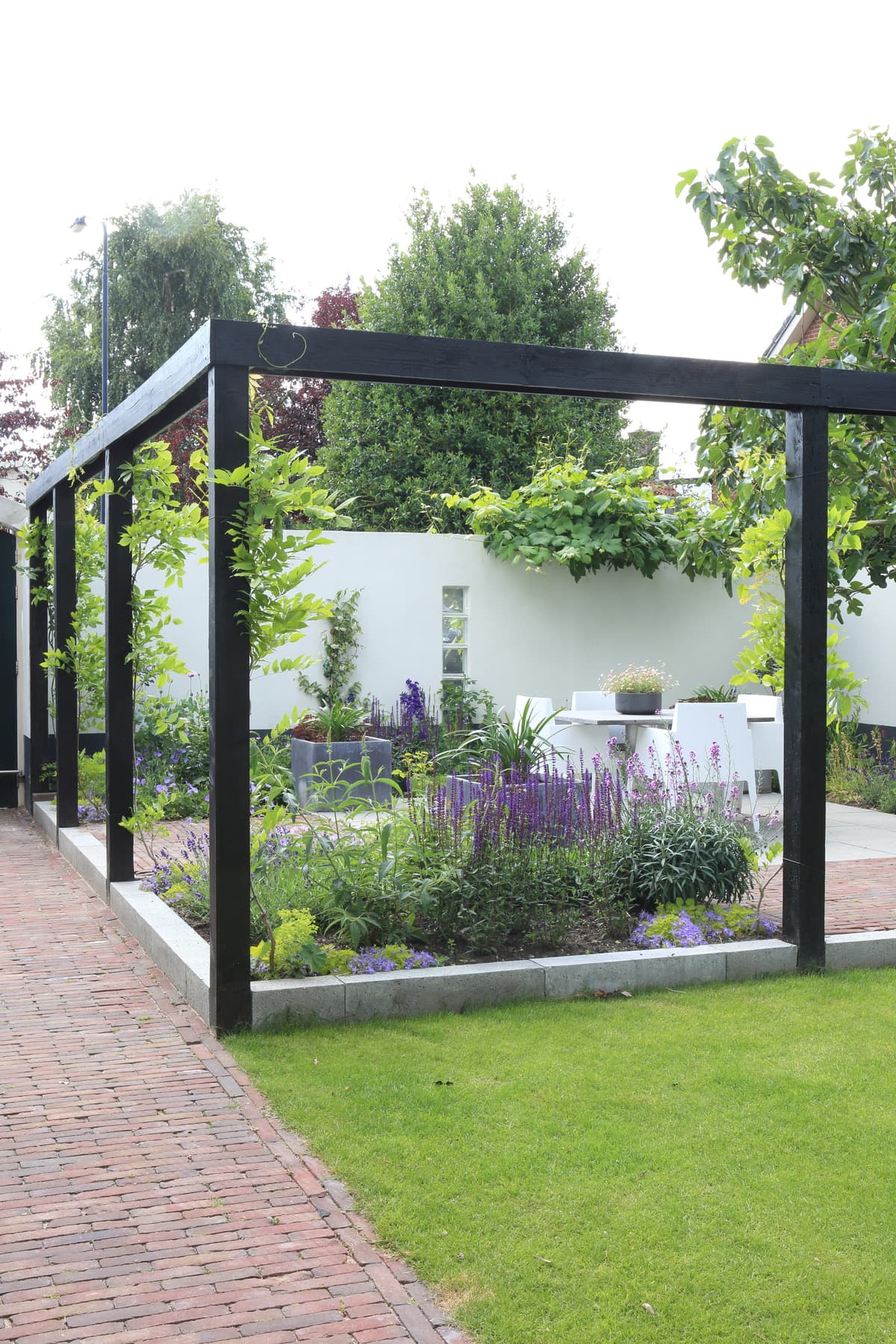 Pergola met paarse bloeiende vaste planten en klassieke klinkerbestrating