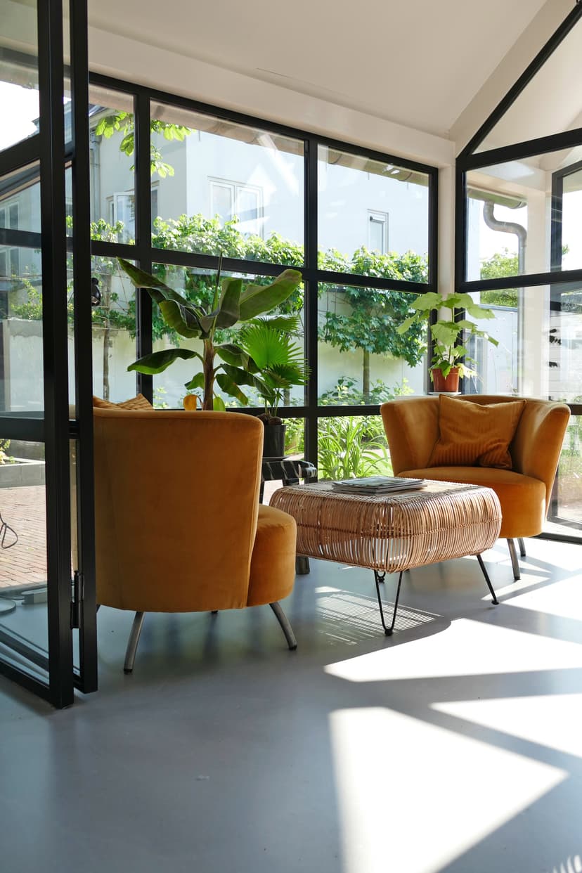 Oranje fauteuils met rieten salontafel bij grote ramen