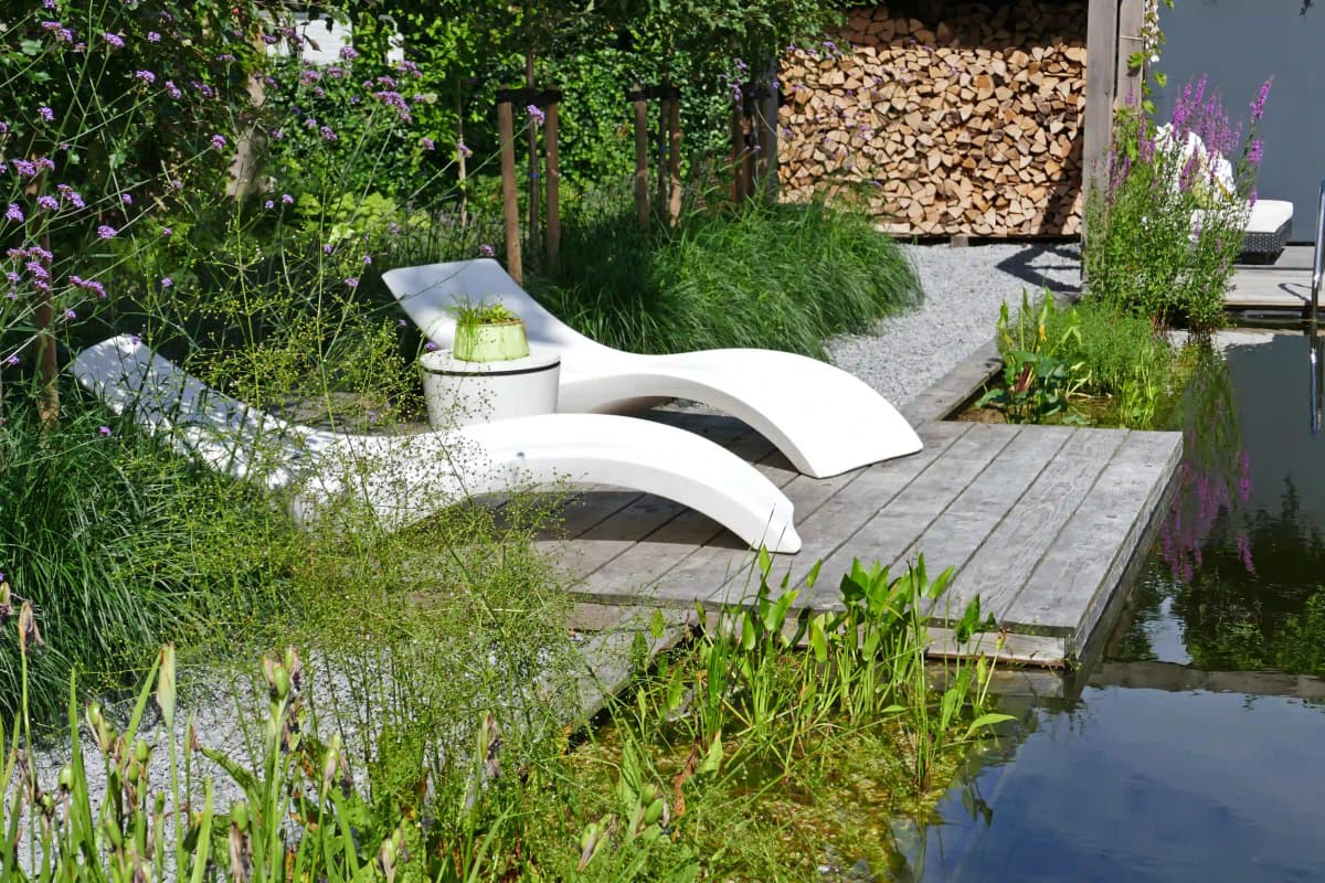 Witte ligbedden op houten vlonder naast natuurlijke zwemvijver met waterplanten