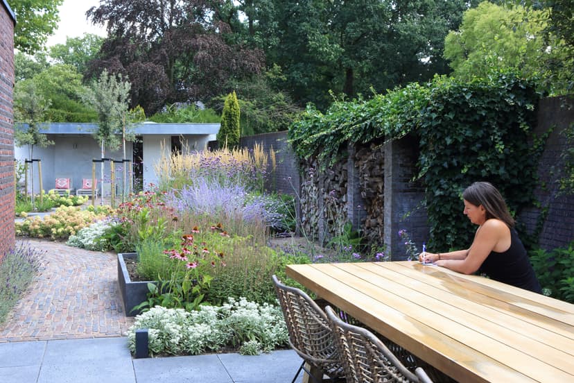 Vrouw aan houten eettafel met uitzicht op kleurrijke tuin