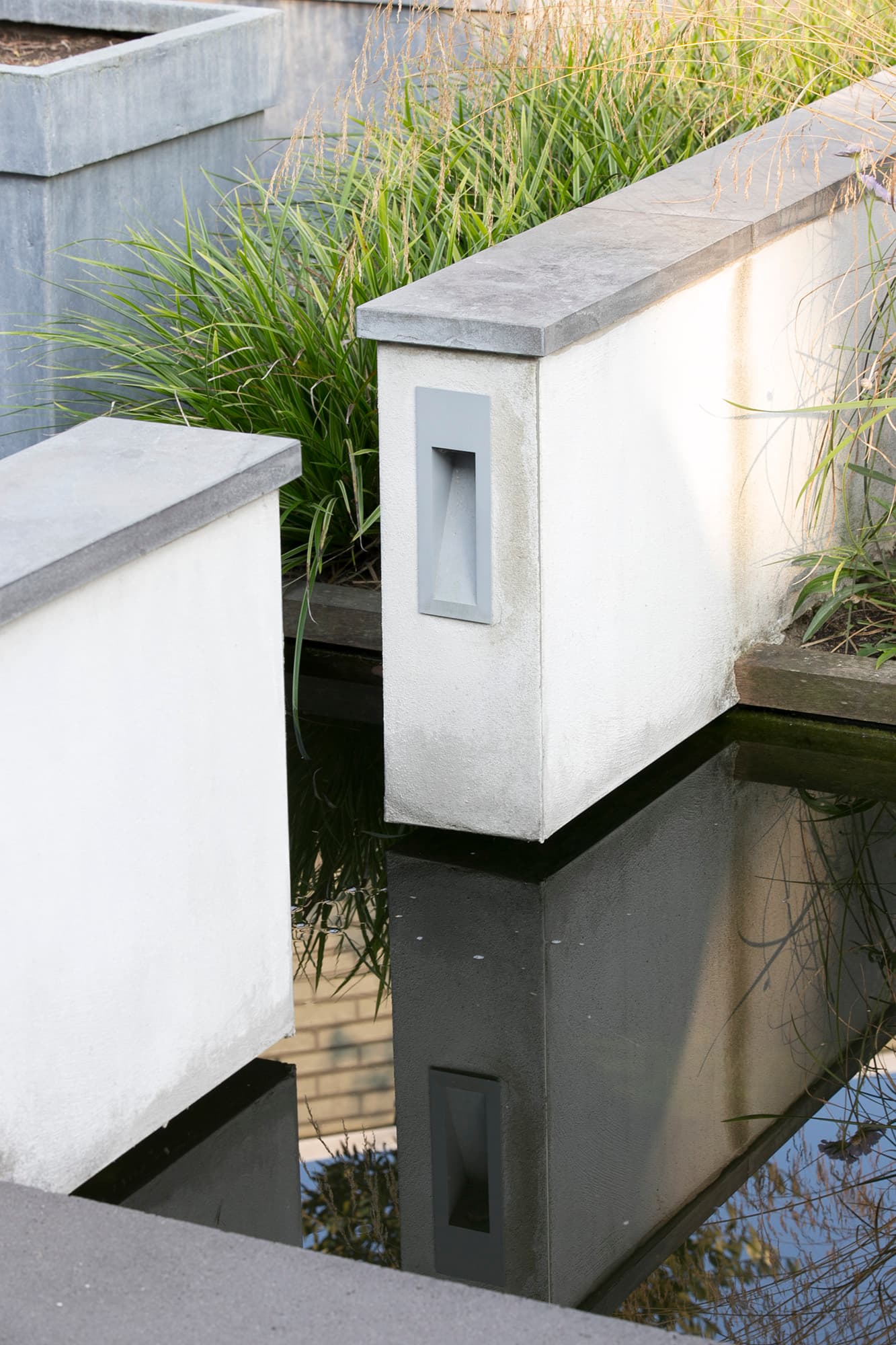 Detail van witte gestucte muurtjes met hardstenen afwerking en ingebouwde verlichting