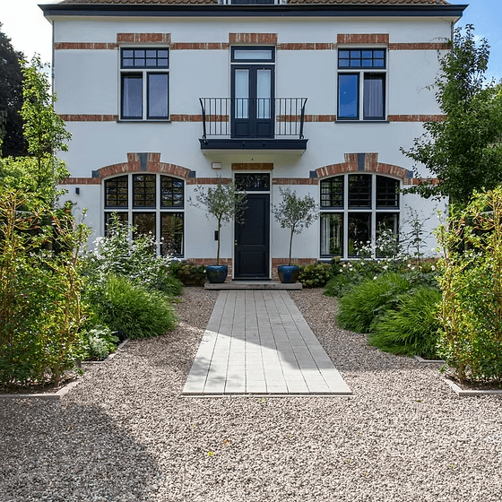 Witte villa met rode bakstenen accenten en voortuin met grindpad en groene beplanting