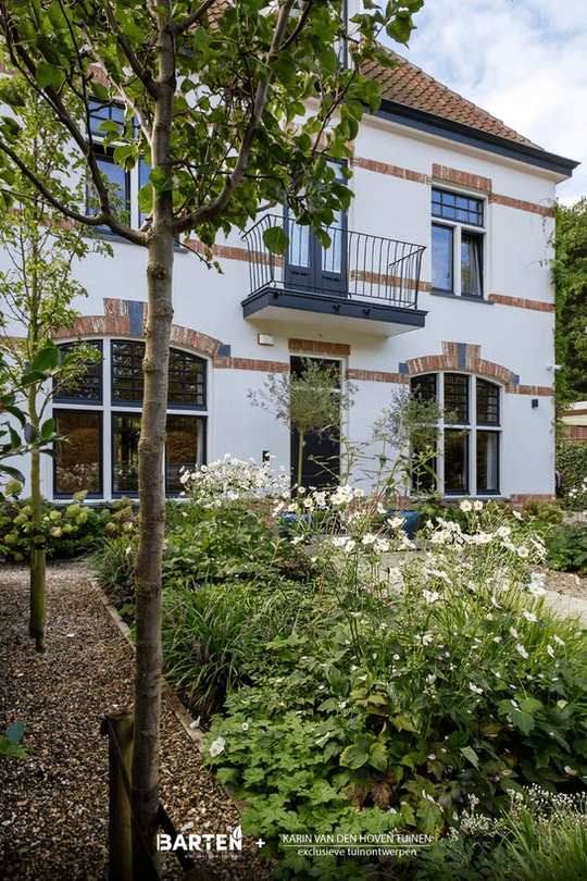 Witte villa met rode bakstenen accenten en voortuin met witte bloemen en grindpad