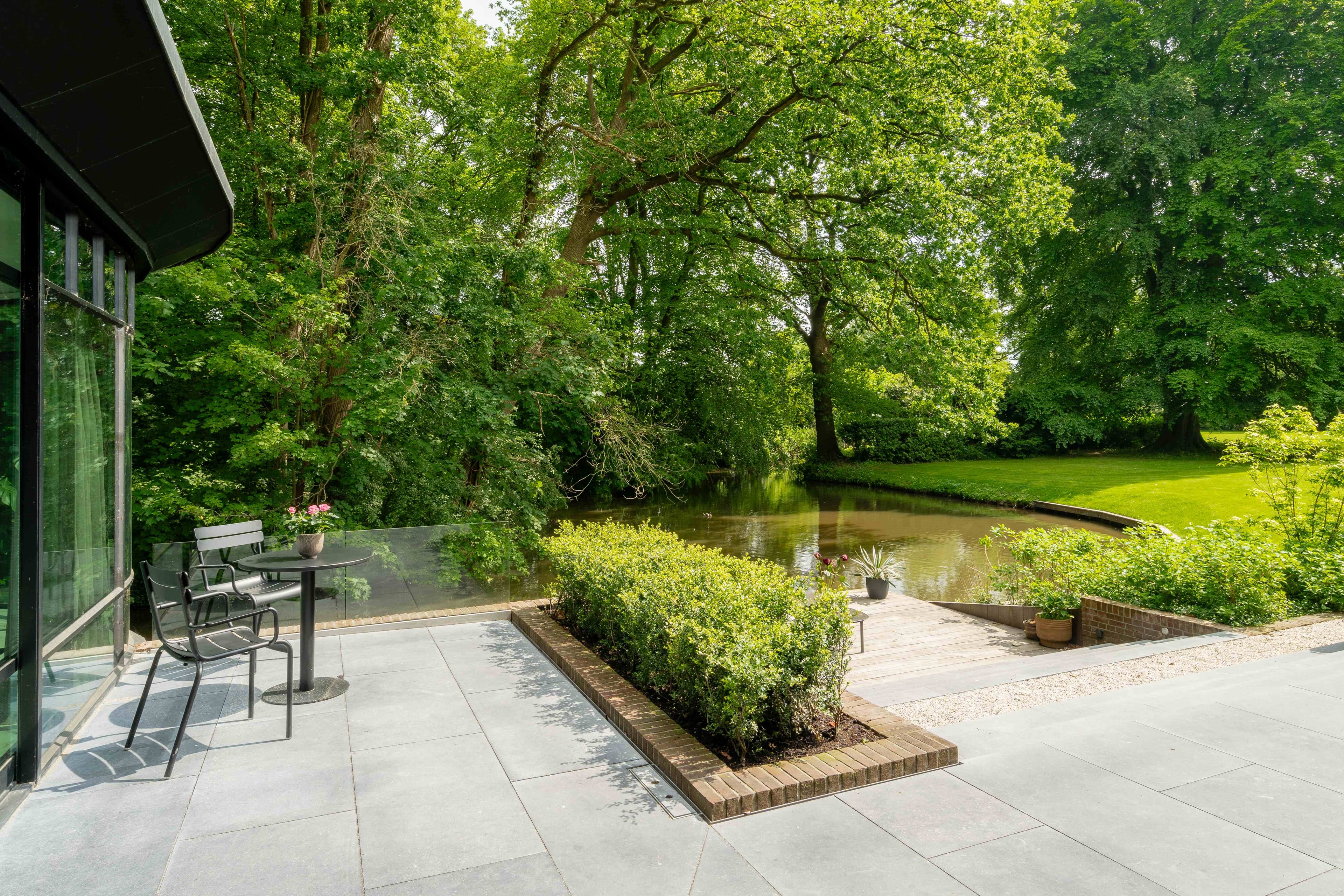 Waterfront terras met geschoren buxus en uitzicht op natuurlijke vijver