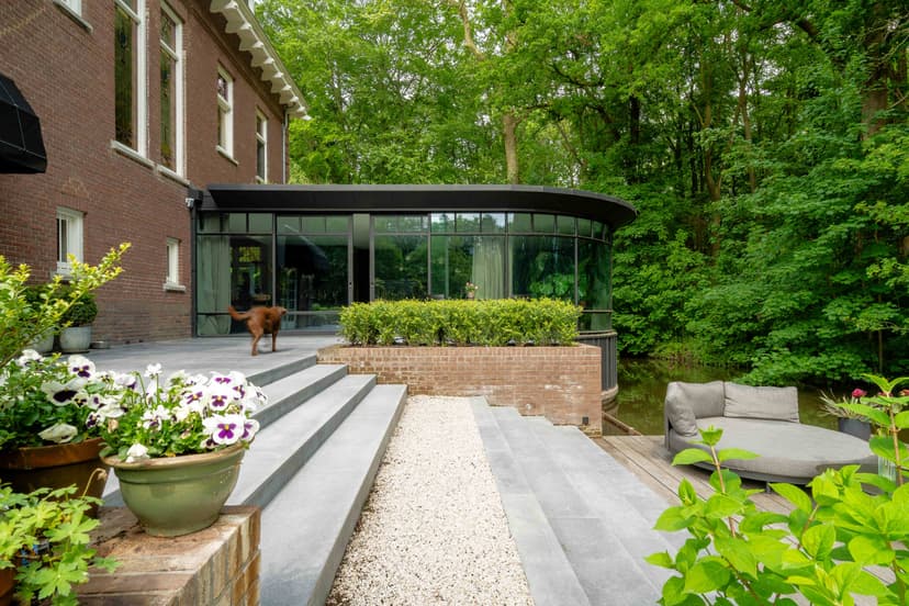 Moderne glazen uitbouw met hond op terras en buitenmeubelen