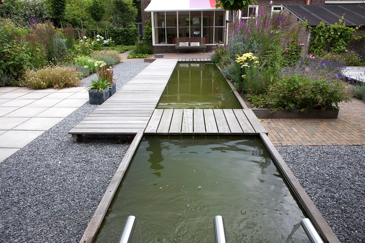 Zicht vanuit huis met houten vlonder over twee vijverdelen met waterpartij
