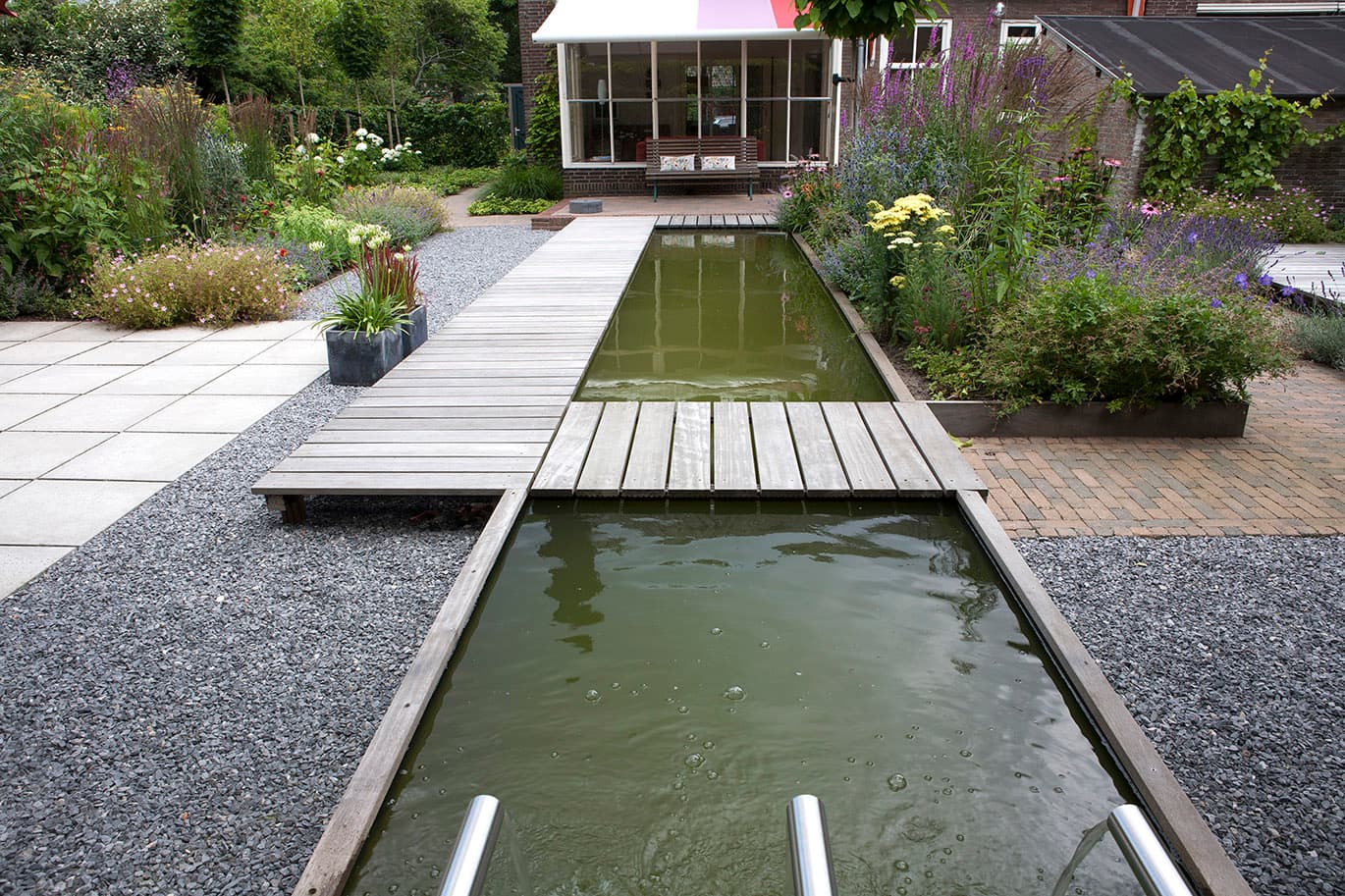 Natuurlijke zwemvijver met houten vlonders en weelderige beplanting met paarse bloemen