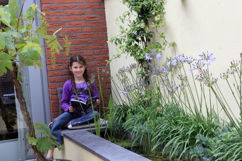 Kind zit lezend op rand van vijver met bloeiende Agapanthus